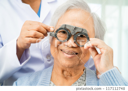 Optometrist checking Asian elderly woman ophthalmic vision eye test and using optical trial frame. 117112748