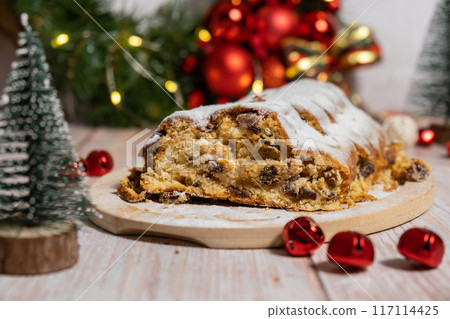 Christmas Stollen in Christmas lights and decoration. Traditional sweet fruit loaf with icing sugar festive pastry dessert. Holiday baking food 117114425