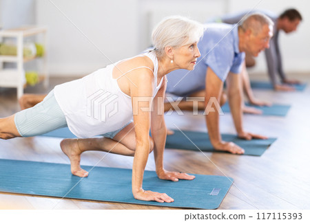 Diligent women and men doing body stretching before yoga class in a fitness studio 117115393
