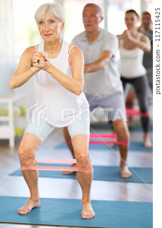 Group of women and men are doing stretching exercise with resistance bands. Good mood and healthy lifestyle concept Group of women and men are doing stretching exercise with resistance bands. Good mood and healthy lifestyle concept 117115425