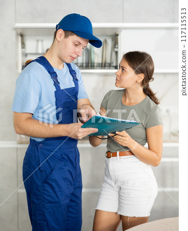 Guy in blue uniform offering young girl to sign papers in the kitchen Guy in blue uniform offering young girl to sign papers in the kitchen 117115513
