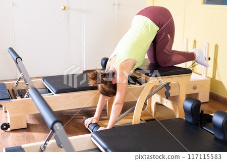 Young woman doing stretching exercises on pilates combo chair Young woman doing stretching exercises on pilates combo chair 117115583