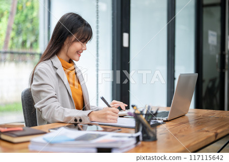 A beautiful Asian businesswoman using a calculator, working on her assignment in the office. 117115642
