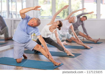 Mature male participant working out practice Parighasana, bolt pose with students group Mature male participant working out practice Parighasana, bolt pose with students group 117115835