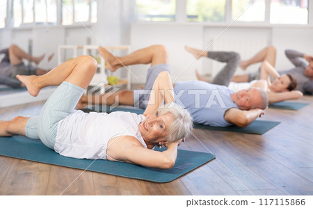 Elderly woman performs exercises to strengthen abdominal muscles during group workout Elderly woman performs exercises to strengthen abdominal muscles during group workout 117115866