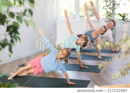 Pleasant little girl practicing side plank pose of yoga with her family Pleasant little girl practicing side plank pose of yoga with her family 117115889