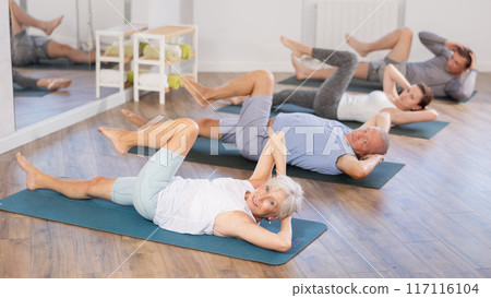 Elderly woman performs exercises to strengthen abdominal muscles during group workout 117116104