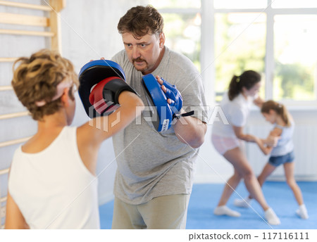 Boy with her trainer father at gym. Boy wearing boxing gloves exercise and punch to pads for boxing 117116111