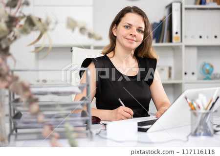 Female office worker sitting at working table and writing 117116118
