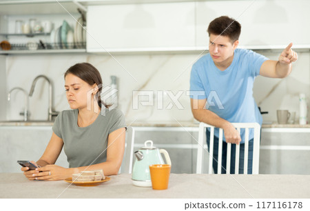 Upset young girl browsing smartphone while irritated boyfriend reprimanding her 117116178