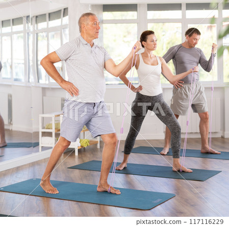 Mature man stretches his body using an expander in group Pilates training 117116229