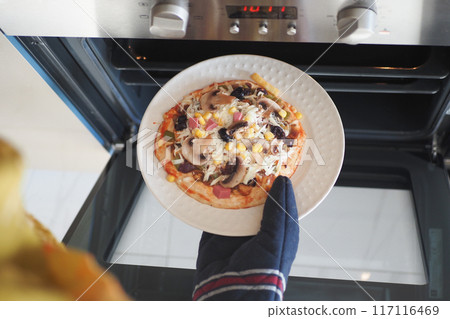 When baking a homemade pizza in the oven, ensure safety by wearing a protective glove on your hand When baking a homemade pizza in the oven, ensure safety by wearing a protective glove on your hand 117116469