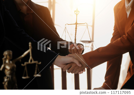 Lawyer shaking hands with a client making about documents, contracts, agreements, cooperation agreements with a female client at the lawyer's desk and a hammer at the table. Lawyer shaking hands with a client making about documents, contracts, agreements, cooperation agreements with a female client at the lawyer's desk and a hammer at the table. 117117095