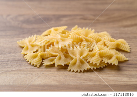 Uncooked farfalle pasta (bow tie shape) on wooden background, Italian food ingredient Uncooked farfalle pasta (bow tie shape) on wooden background, Italian food ingredient 117118016