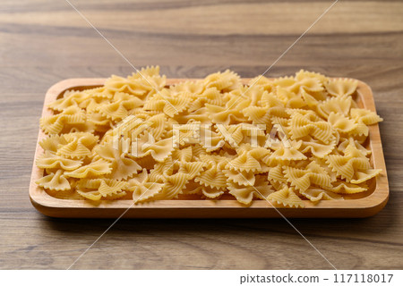 Uncooked farfalle pasta (bow tie shape) in wooden plate, Italian food ingredient 117118017