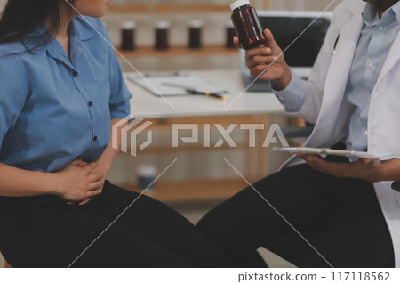 Confident doctor man holding a pill bottle and writing while talking with senior patient and reviewing his medication at office room. 117118562