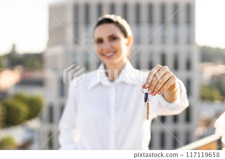 Smiling woman holding keys outdoors in urban setting Smiling woman holding keys outdoors in urban setting 117119658