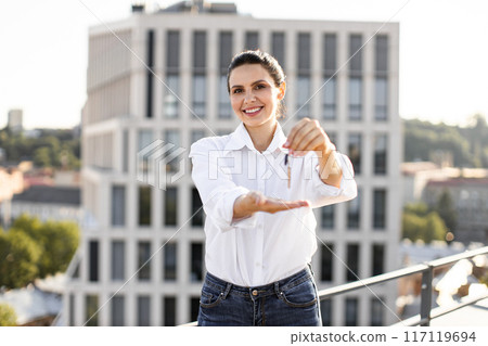 Happy woman holding keys on rooftop in city 117119694