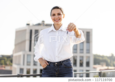 Smiling woman holding keys on urban rooftop 117119700