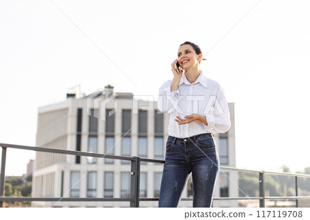 Businesswoman on phone outside office building smiling confidently Businesswoman on phone outside office building smiling confidently 117119708