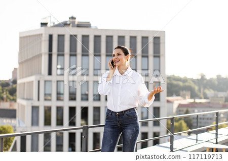 Businesswoman talking on phone on rooftop with city backdrop 117119713