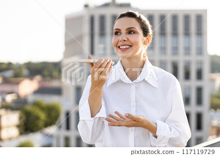 Businesswoman using smartphone voice assistant outdoors in urban setting 117119729