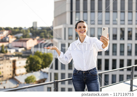 Woman taking selfie on rooftop with modern cityscape background Woman taking selfie on rooftop with modern cityscape background 117119753