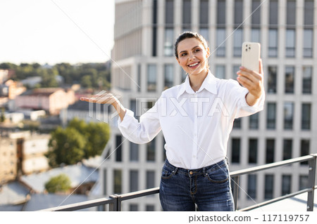 Smiling woman taking selfie on rooftop in urban setting 117119757