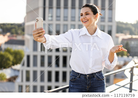 Smiling woman taking selfie on rooftop during sunny day 117119759