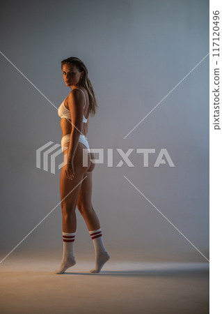 Beautiful athletic girl in socks and underwear posing in a photo studio. Dramatic light. Vertical photographs. 117120496