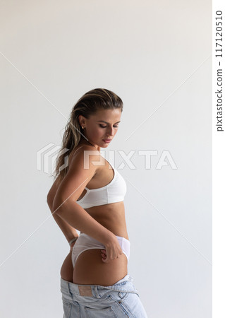 Beautiful blonde in white lingerie and jeans posing on white background 117120510