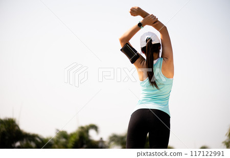 Young fitness woman runner stretching arm before run in the park. Outdoor exercise activities concept. 117122991