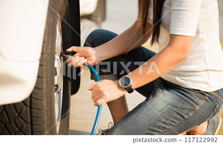 Woman driver checking air pressure and filling air in the tires close up. 117122992