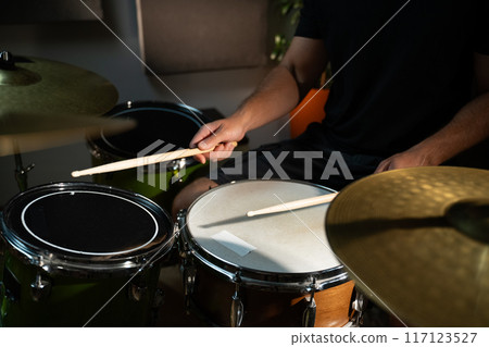 A close-up view of a drummer's hands as they play a snare drum during a practice session. The drummer is wearing a black t-shirt and is sitting behind a drum set. A close-up view of a drummer's hands as they play a snare drum during a practice session. The drummer is wearing a black t-shirt and is sitting behind a drum set. 117123527