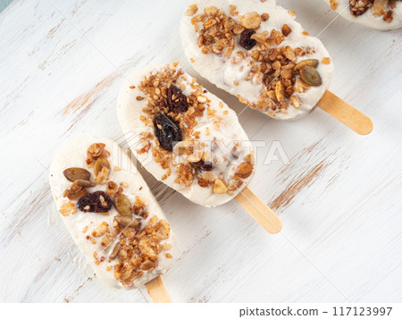 Homemade greek yogurt popsicles with granola on white wooden board 117123997