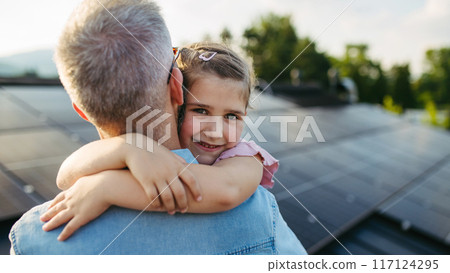 Father with girl on roof with solar panels, hugging. Rooftop solar or photovoltaic system. Sustainable future for next generation. Father with girl on roof with solar panels, hugging. Rooftop solar or photovoltaic system. Sustainable future for next generation. 117124295
