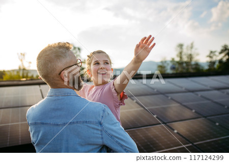 Father with girl on roof with solar panels, hugging, looking at the sky. Rooftop solar or photovoltaic system. Sustainable future for next generation. Father with girl on roof with solar panels, hugging, looking at the sky. Rooftop solar or photovoltaic system. Sustainable future for next generation. 117124299