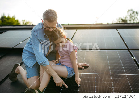 Dad and girl on roof with solar panels, learning about solar energy. Rooftop solar or photovoltaic system. Sustainable future for next generation. Dad and girl on roof with solar panels, learning about solar energy. Rooftop solar or photovoltaic system. Sustainable future for next generation. 117124304