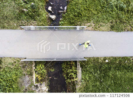 Aerial view of a runner running across bridge in park on a jogging path. Morning running training. Aerial view of a runner running across bridge in park on a jogging path. Morning running training. 117124506