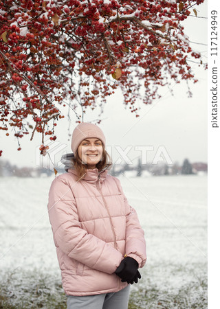 Winter Elegance: Portrait of a Beautiful Girl in a Snowy European Village. Winter lifestyle portrait of cheerful pretty girl. Smiling and having fun in the snow park. Snowflakes falling down Winter Elegance: Portrait of a Beautiful Girl in a Snowy European Village. Winter lifestyle portrait of cheerful pretty girl. Smiling and having fun in the snow park. Snowflakes falling down 117124949