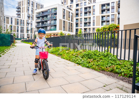 Little girl rides a two-wheeled bicycle Ii the courtyard of apartment buildings in summer, Europe 117129114