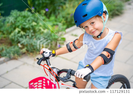 Portrait of little girl rides a two-wheeled bicycle Ii the courtyard of apartment buildings in summer, Europe 117129131
