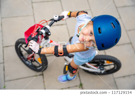Top view of little girl rides a two-wheeled bicycle Ii the courtyard of apartment buildings in summer, Europe Top view of little girl rides a two-wheeled bicycle Ii the courtyard of apartment buildings in summer, Europe 117129154