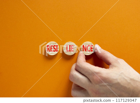 Resilience symbol. Concept word Resilience on beautiful wooden circles. Businessman hand. Beautiful orange background. Business resilience concept. Copy space. 117129347