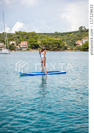 Young woman paddling on a paddle surfboard near yachts in Croatia sea bay 117129632