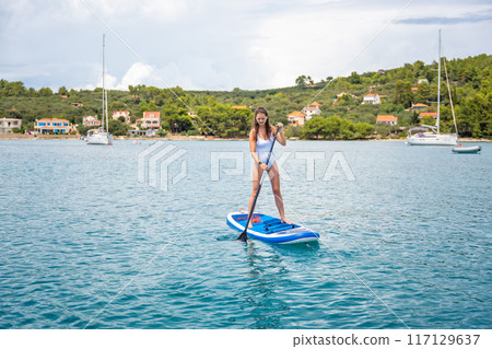 Young woman paddling on a paddle surfboard near yachts in Croatia sea bay 117129637