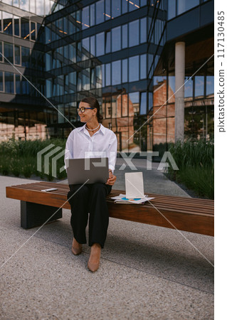 A Business Professional Engaged in Work Outdoors While Using Their Laptop for Tasks A Business Professional Engaged in Work Outdoors While Using Their Laptop for Tasks 117130485