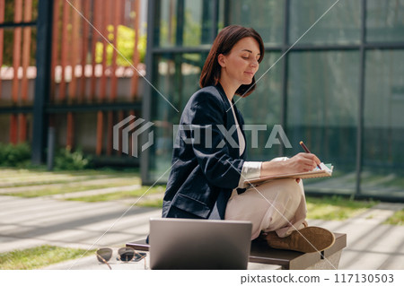 A woman is working outdoors with a laptop in a professional and relaxed environment A woman is working outdoors with a laptop in a professional and relaxed environment 117130503