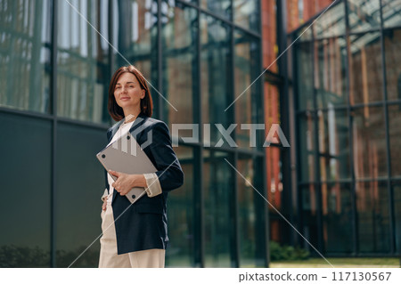 A confident businesswoman is working on a laptop outside a contemporary office building 117130567