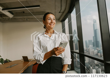 A professional woman confidently working in a modern office setting using her smartphone A professional woman confidently working in a modern office setting using her smartphone 117130623